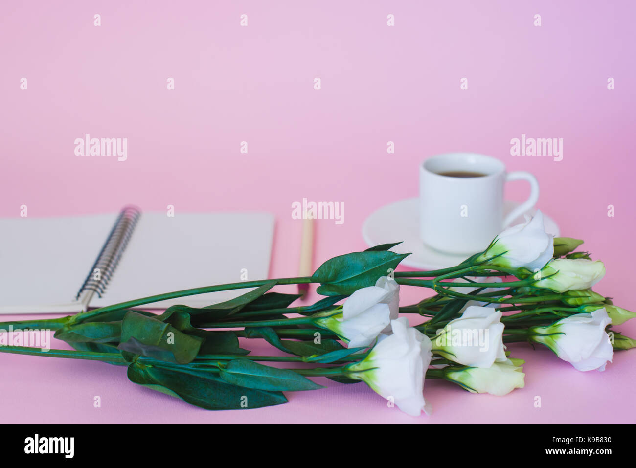 Niederlassung von Blumen auf dem Hintergrund einer Tasse Kaffee, Notizblock und Stift. Fokus auf Blumen. Stockfoto