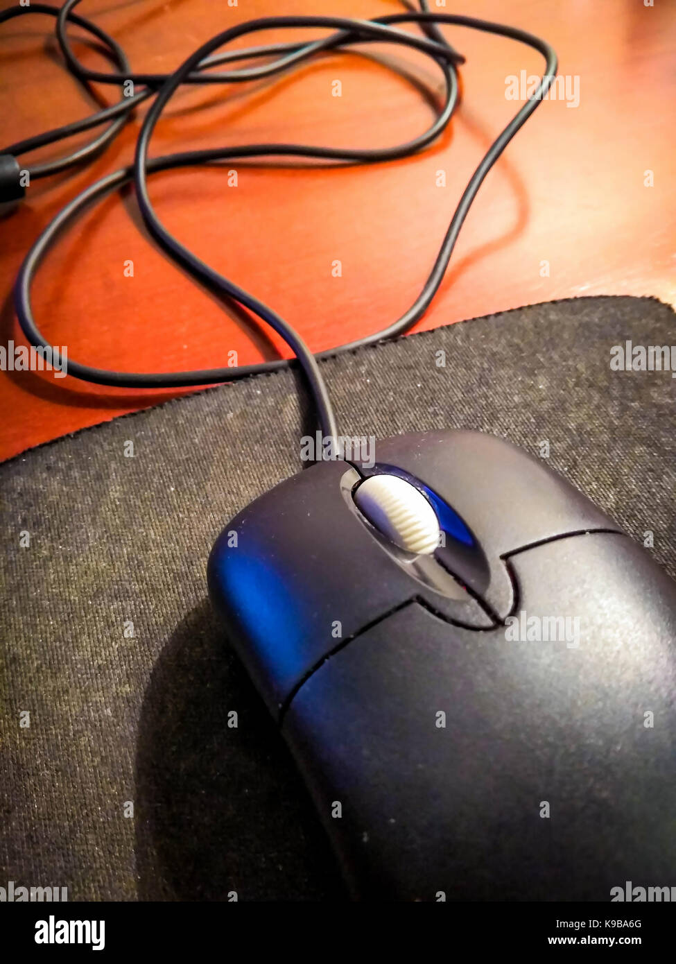 Computer verdrahtet schwarze Maus auf eine Gummimatte liegen auf einem braunen Holztisch Stockfoto