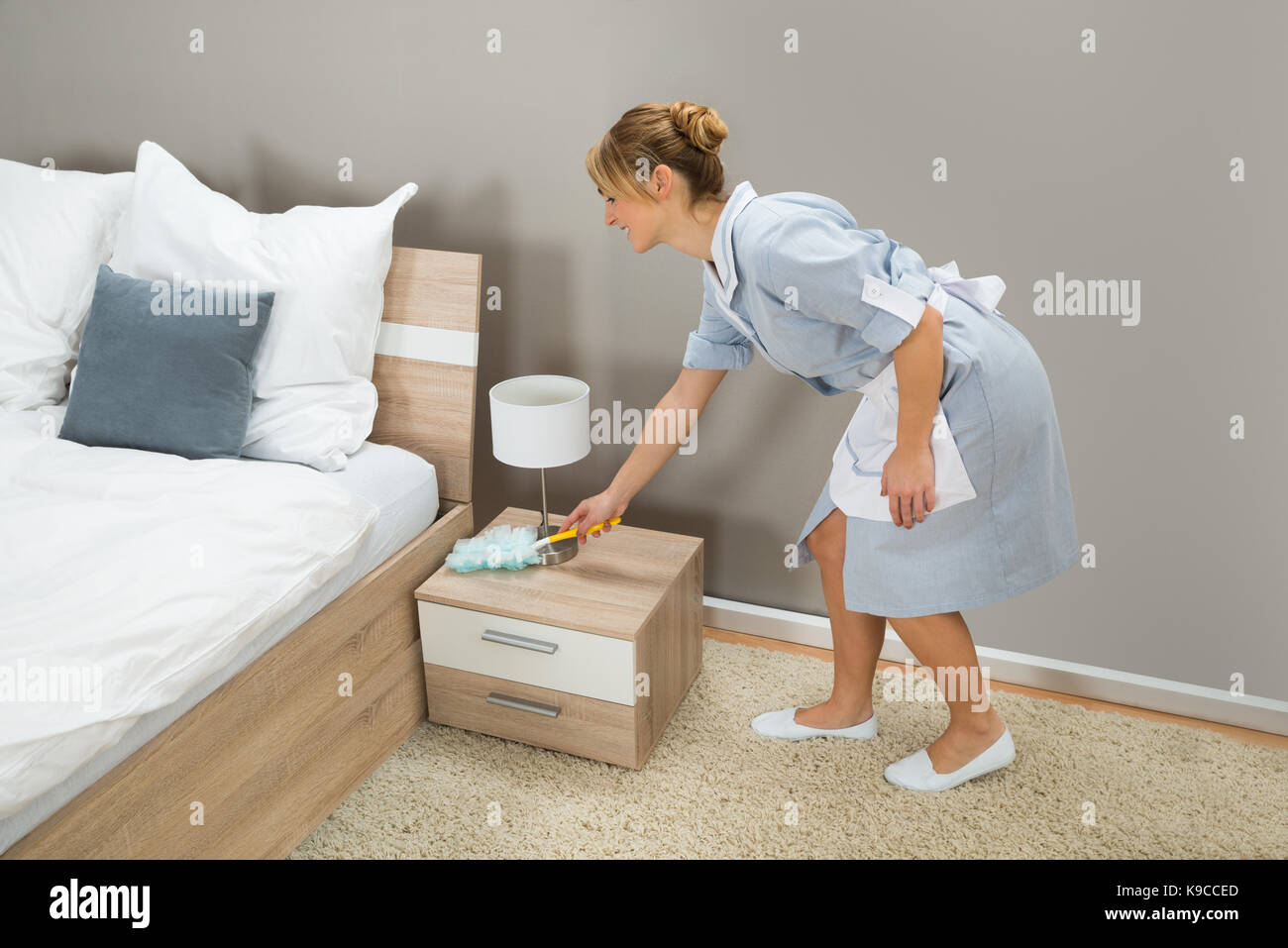 Junge glücklich Zimmermädchen Reinigung Staub mit Staubwedel im Hotel Zimmer Stockfoto