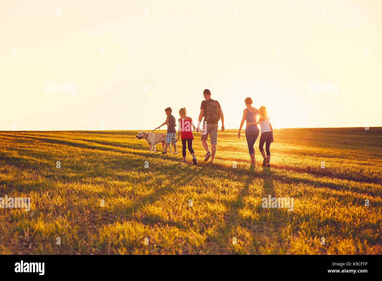 Sommer auf dem Land. Silhouetten der Familie mit Hund auf der Fahrt in den Sonnenuntergang. Stockfoto