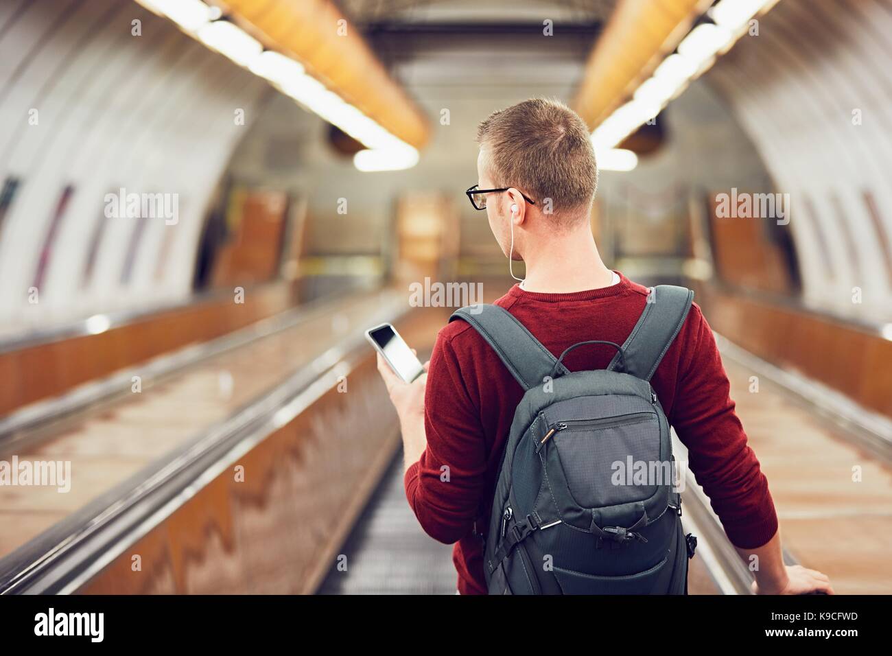Anreise mit öffentlichen Verkehrsmitteln. Junger Mann Musik hören über Kopfhörer auf der Rolltreppe zur U-Bahn. Stockfoto