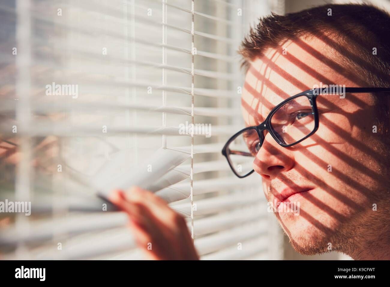 Neugierig Mann mit Brille schauen durch eine Jalousie. Themen Neugierde, Überwachung oder die Sehkraft. Stockfoto