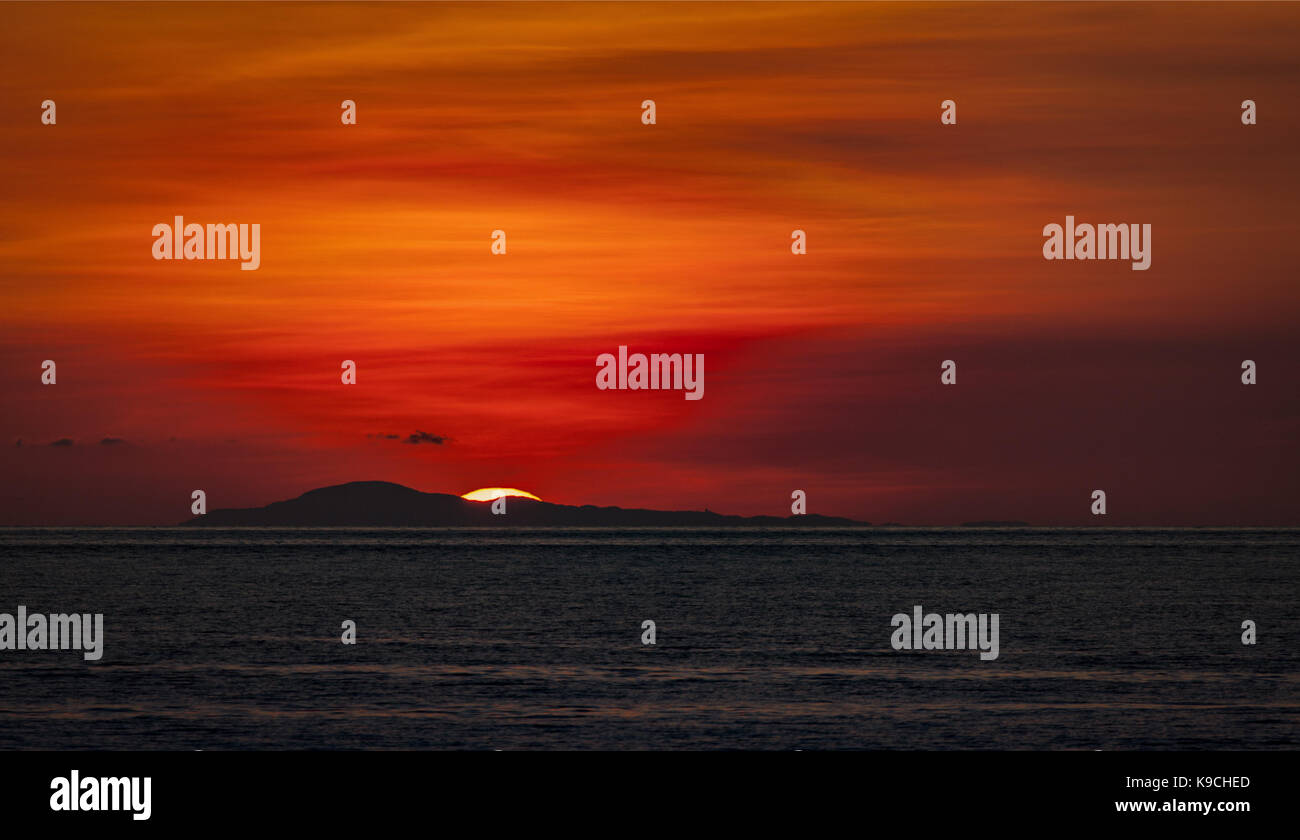 Letzter Blick auf die untergehende Sonne mit tiefen Rot, Gold und orange Farben in der Verde Insel Strait aus Puerto Galera, Mindoro, Philippinen. Stockfoto