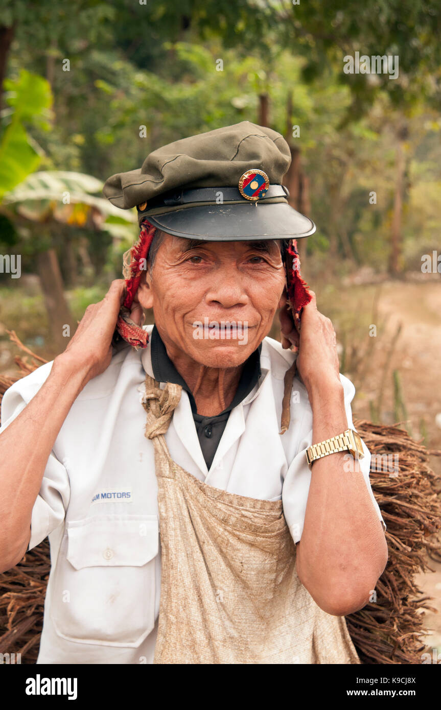Vertikales Porträt eines alten laotischen Soldaten mit seiner alten Armeekappe, der Holz aus dem Wald im Nordosten Laos trägt Stockfoto