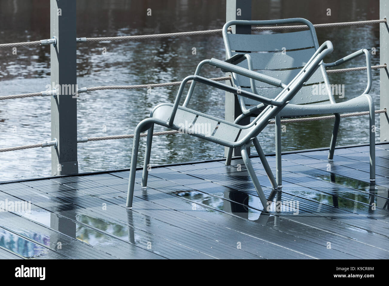 Zwei Außen-graues Metall Stühle stehen auf nassen Pier Stockfoto