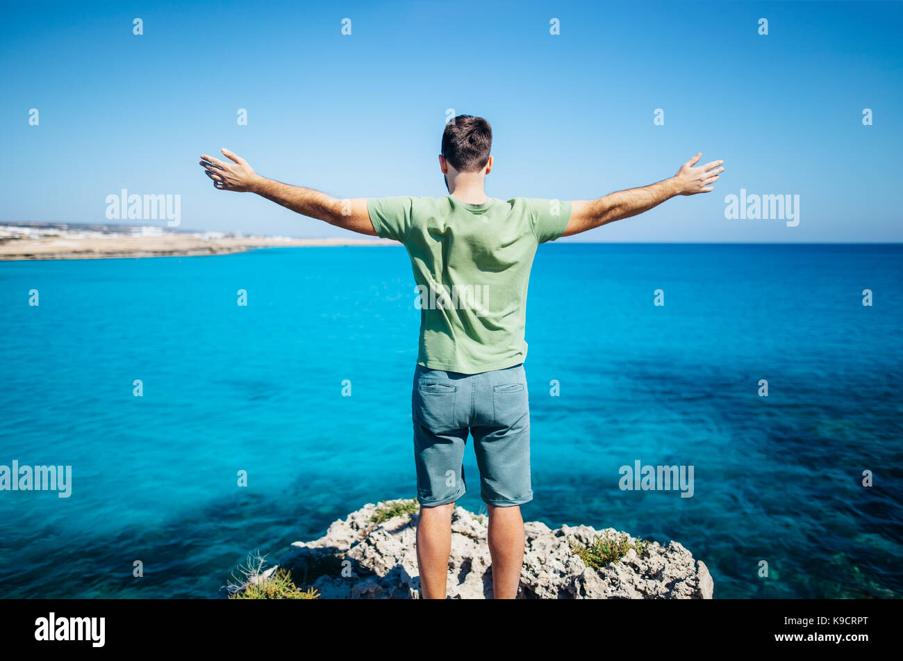 Rückansicht der junge Mann seine Hände auf der Klippe über dem Meer. Entspannen Konzept. Stockfoto
