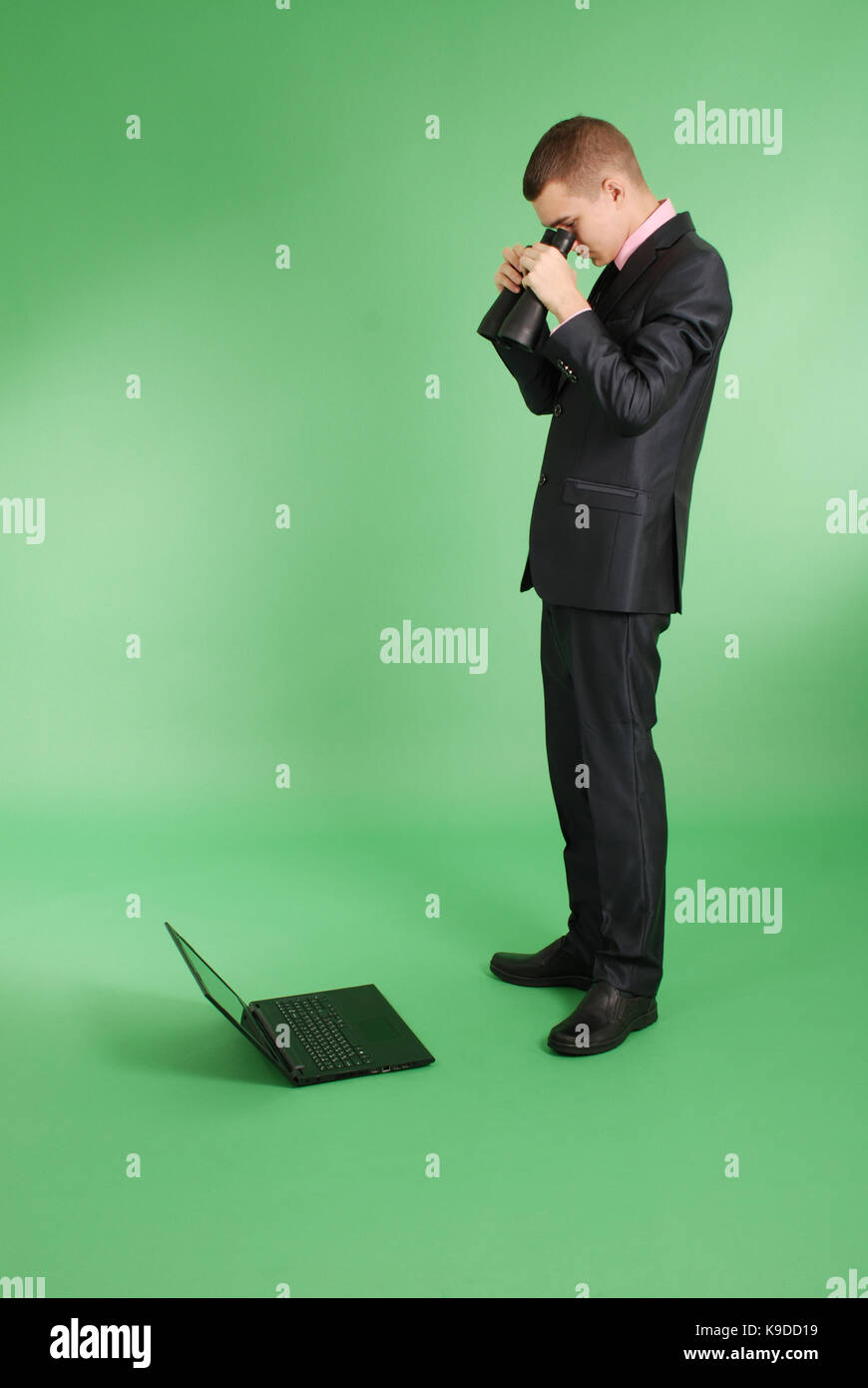 Volle Länge Portrait von zuversichtlich reife Geschäftsmann, die durch ein Fernglas in Laptop in formals stehend über grünen Hintergrund isoliert sieht Stockfoto