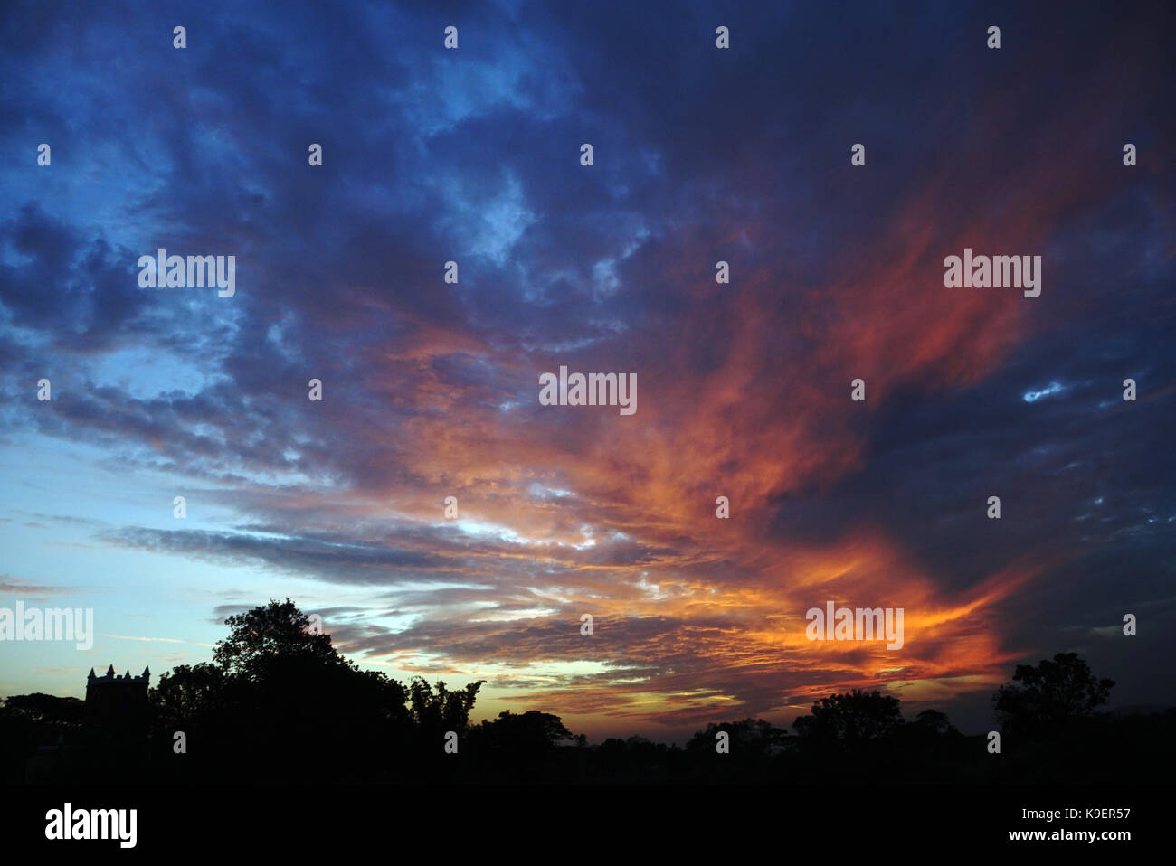 Die leuchtenden Farben der Wolken und die Silhouette der Bäume und einer Kirche. Stockfoto