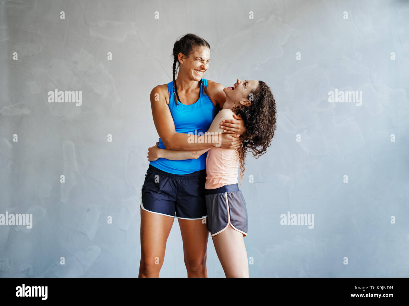 Zwei junge Freundinnen in Sportswear ständigen Arm in Arm zusammen in einer Turnhalle lachen Stockfoto