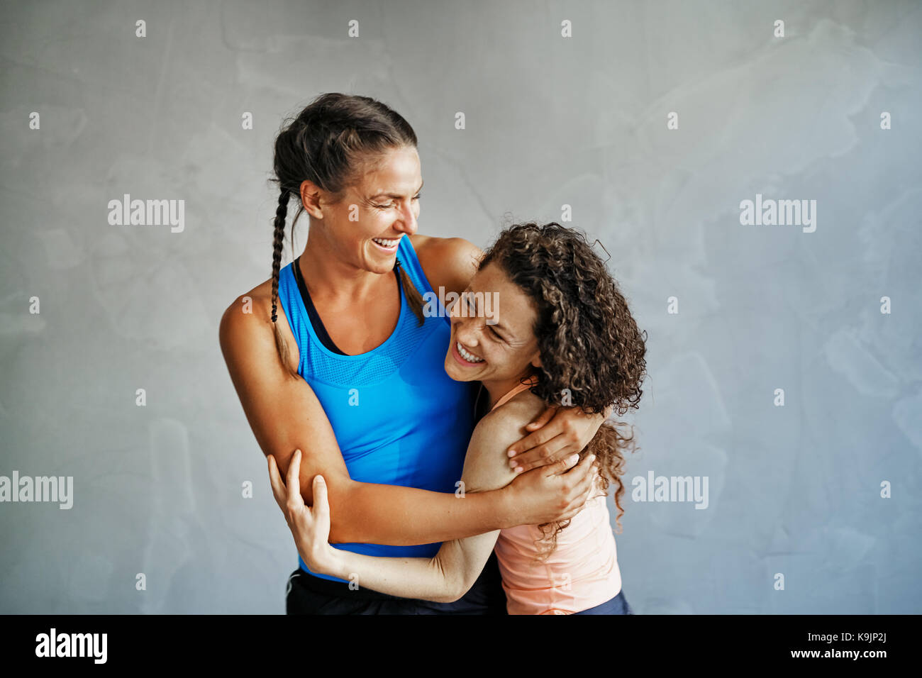 Zwei junge Freundinnen in Sportswear ständigen Arm in Arm zusammen in einer Turnhalle lachen Stockfoto