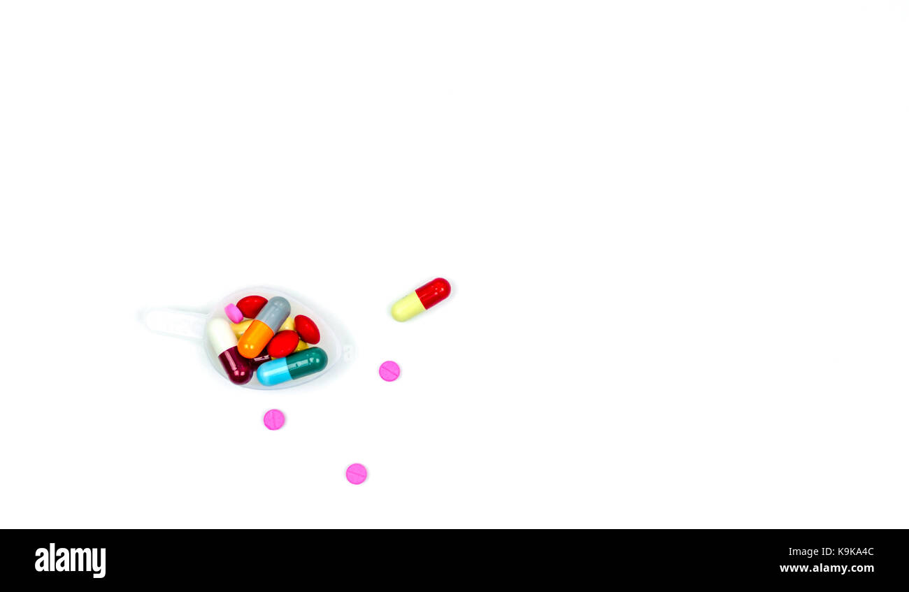 Bunte Pillen, Tabletten und Kapseln in Kunststoff Teelöffel und einige von Ihnen verteilt auf weißem Hintergrund mit Kopie Raum, nur Ihren eigenen Text hinzu. Stockfoto