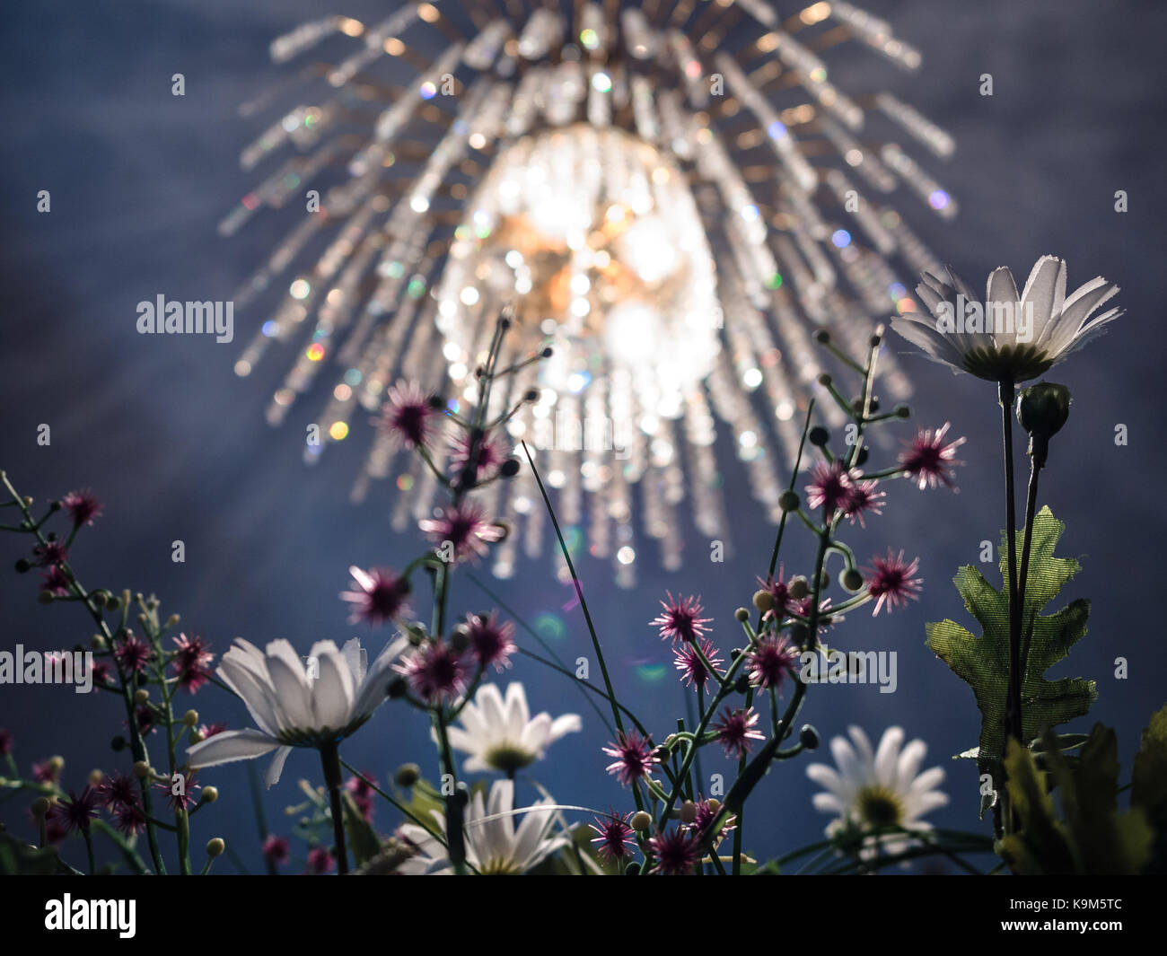 Kronleuchter aus Kristall mit goldenem Licht und künstliche Blumen. Stockfoto