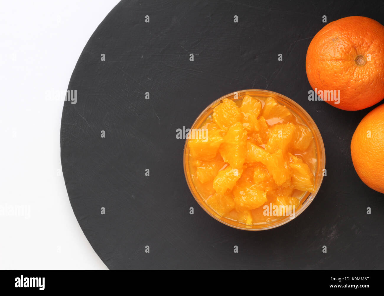 Orange Scheiben in Pudding Schüssel auf schwarzen Schiefer mit zwei ganze Orangen auf der Seite. Ansicht von oben essen Hintergrund mit Platz für Text Stockfoto