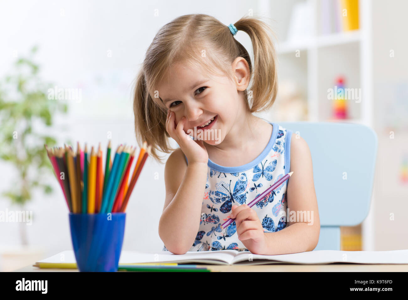 Süße kleine Mädchen Zeichnung mit bunten Stiften auf Papier. Hübsches Kind malen in Innenräumen zu Hause, in der Kindertagesstätte oder Kindergarten Stockfoto