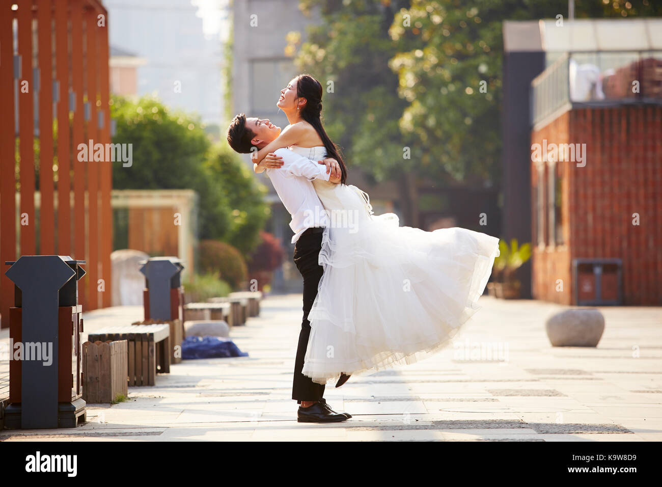 Asiatische frisch vermählte Braut und Bräutigam feiern Ehe und Umarmen außerhalb eines Gebäudes. Stockfoto