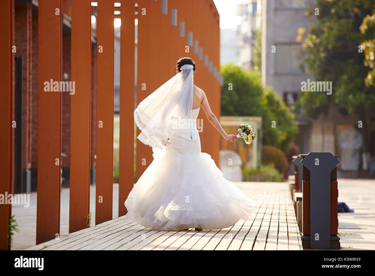 Asiatische Braut im weissen Brautkleid zu Fuß mit einem Blumenstrauß, Ansicht von hinten. Stockfoto