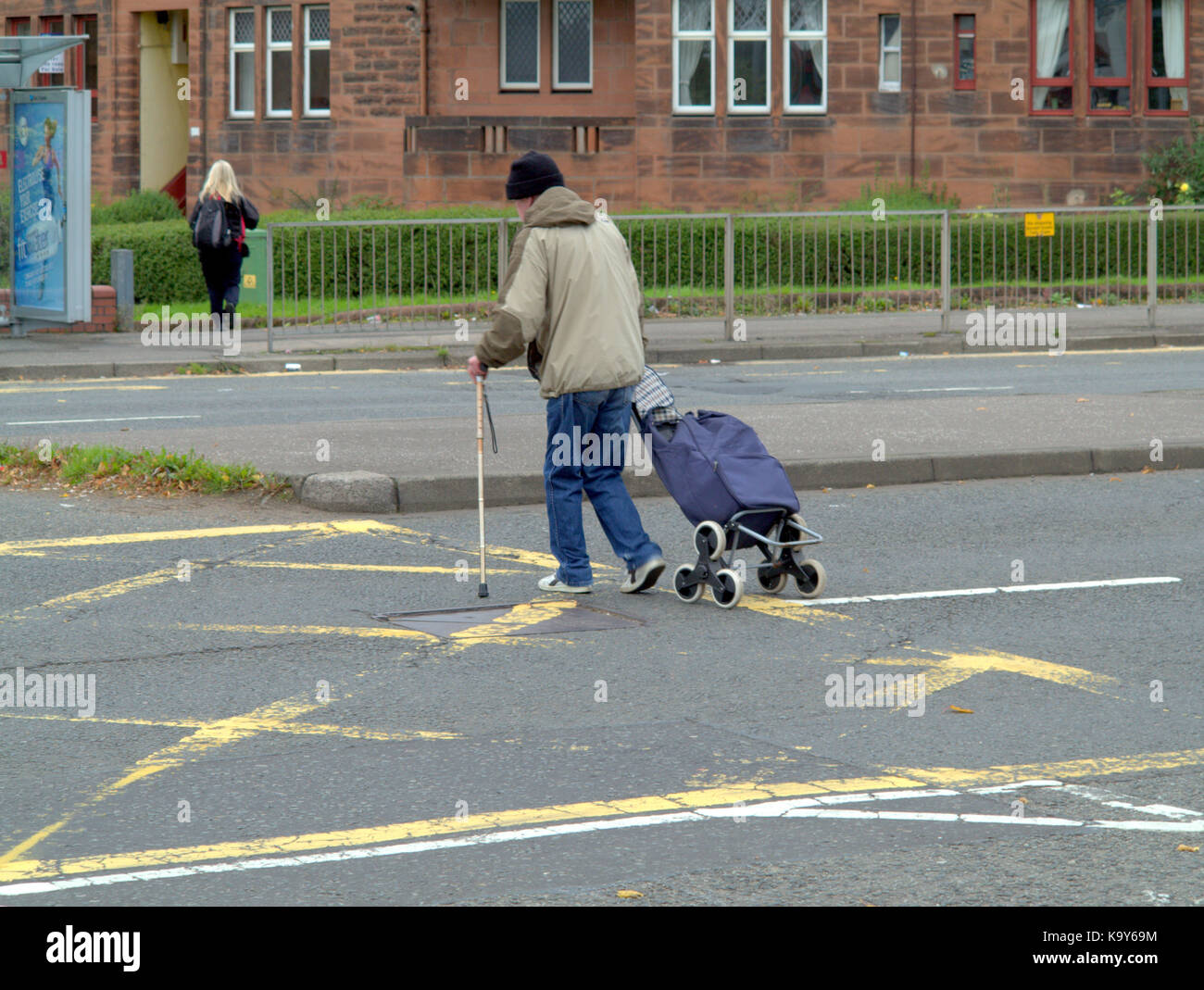 Armut Gesundheit Mann mit Stock und Trolley Crossing Road Glasgow Stockfoto