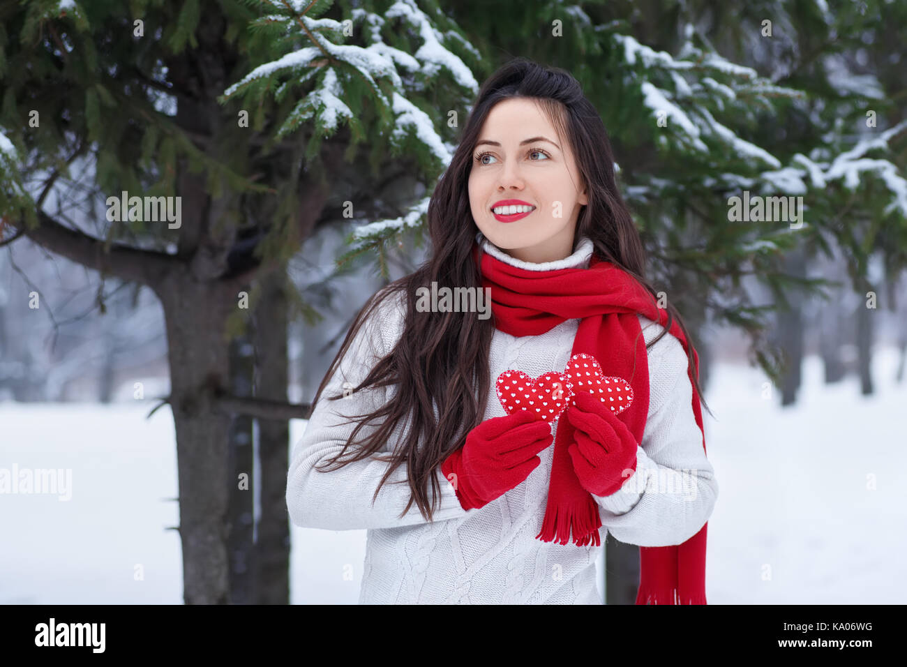 Mädchen im Winter Wald mit roten Herzen in die Hände. Winterurlaub, Valentinstag, Personen Konzept. Winter outdoor Porträt der jungen Frau in Pullover Stockfoto