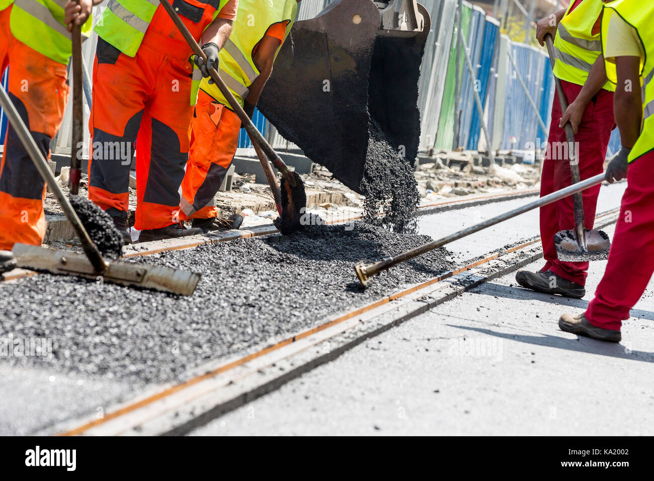 Team der Arbeiter den heißen Asphalt auf einer Straße entlang der Tram Car Eisenbahnstrecken. Straße Bauarbeiter mit Schaufeln im schützenden Uniformen und ein Stockfoto