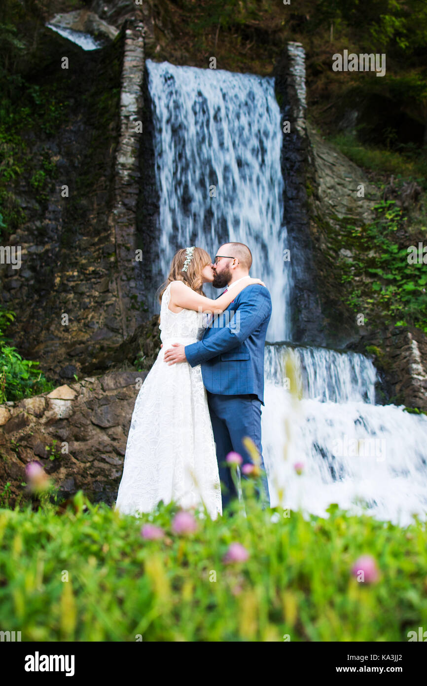 Braut und Bräutigam küssen vor einem Wasserfall Stockfoto