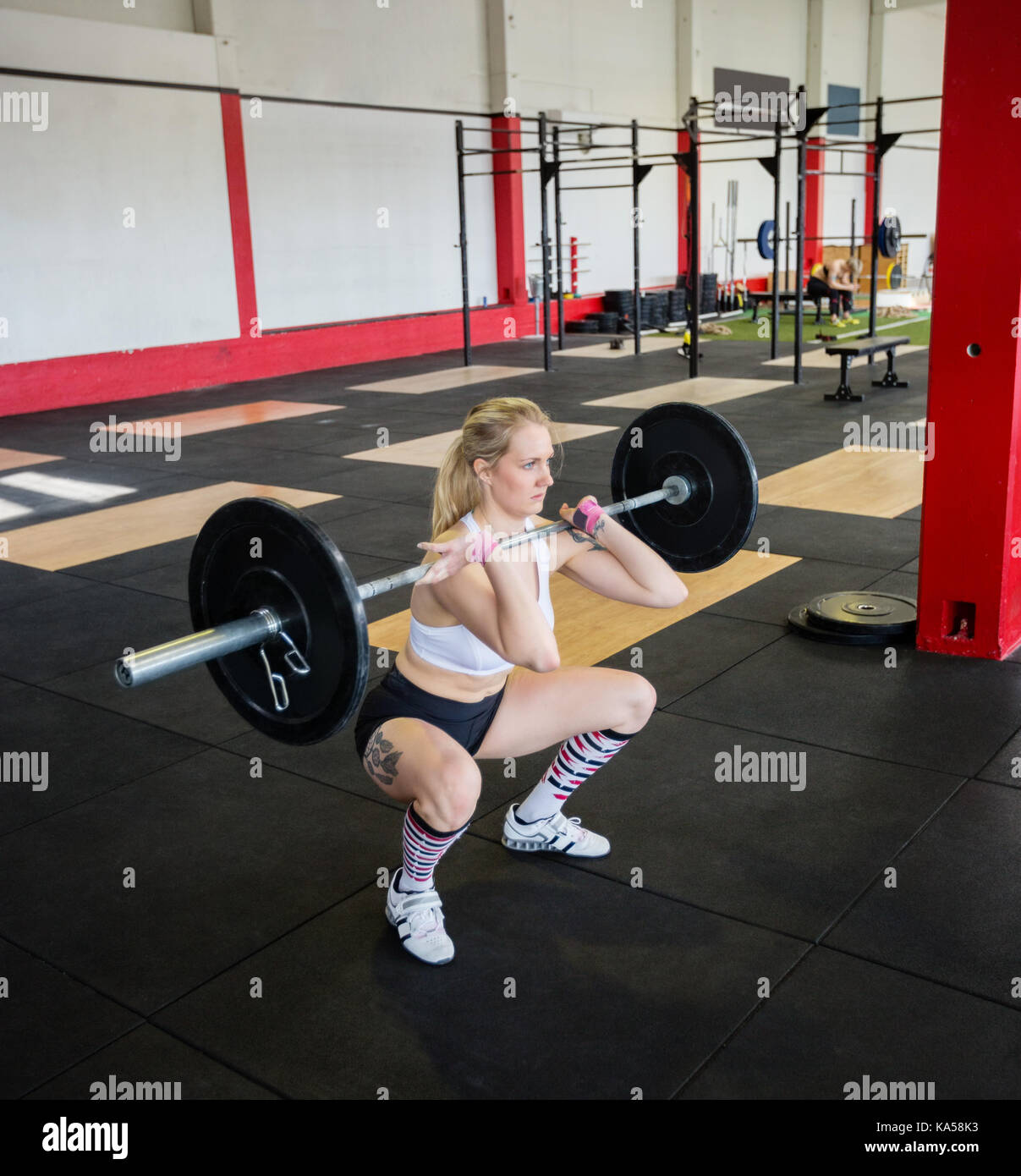 Frau In Sportswear Hockend beim Anheben der Langhantel Stockfoto