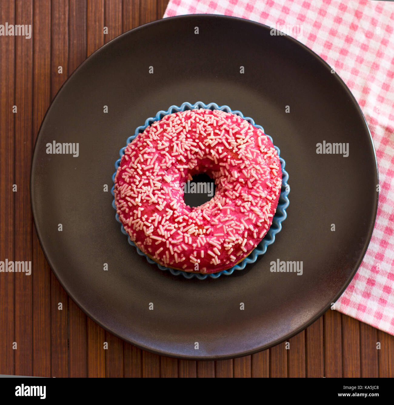 Hell rosa Donut auf braunem Holz- Hintergrund. Mit rosa-karierten Tuch Stockfoto