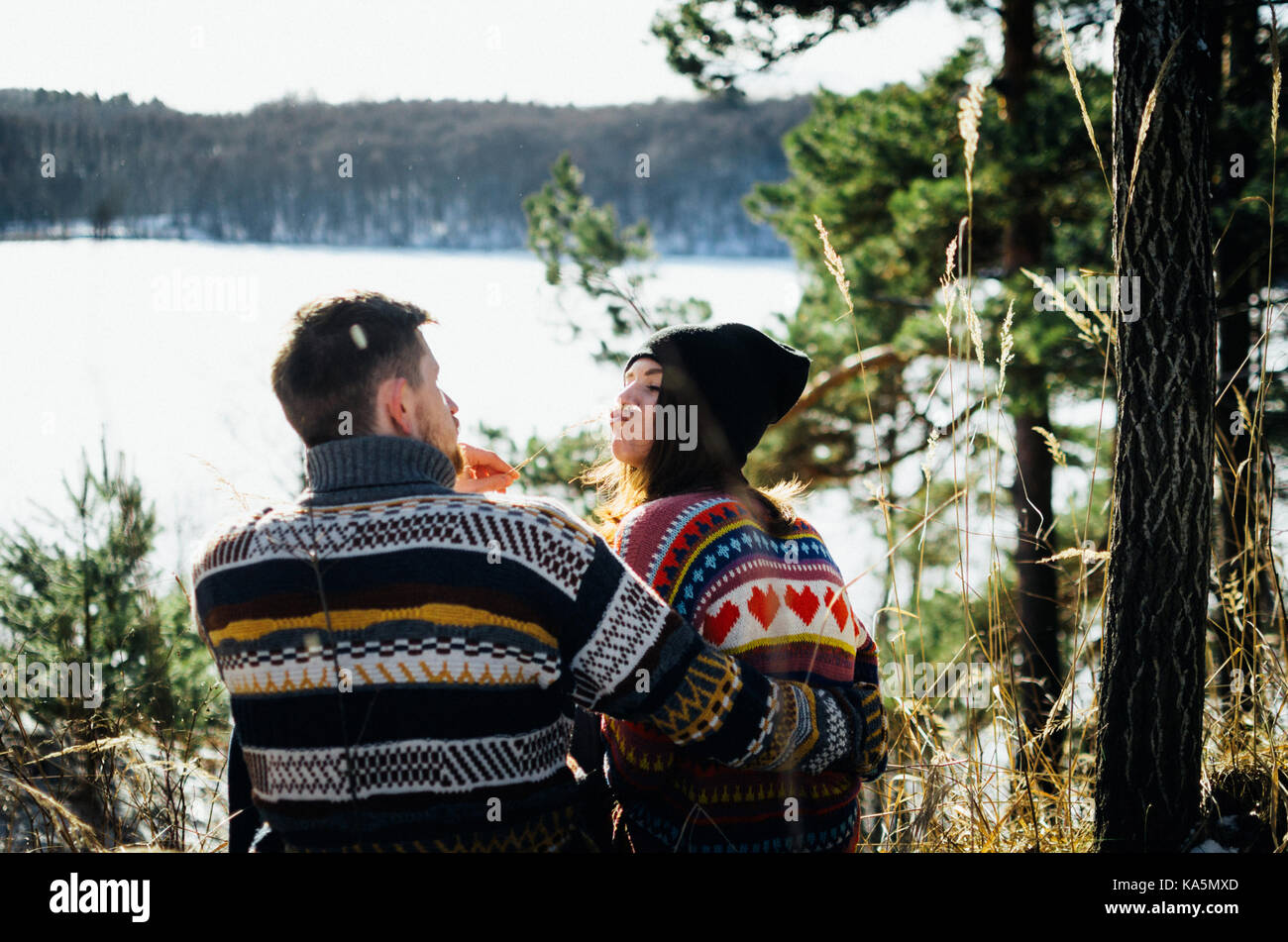 Freudige lustig Paar in warme Kleidung vor gefrorenen See zwischen Wald. Junger Mann umarmt die Frau. Das Konzept der erfolgreichen Beziehung und glücklich Stockfoto