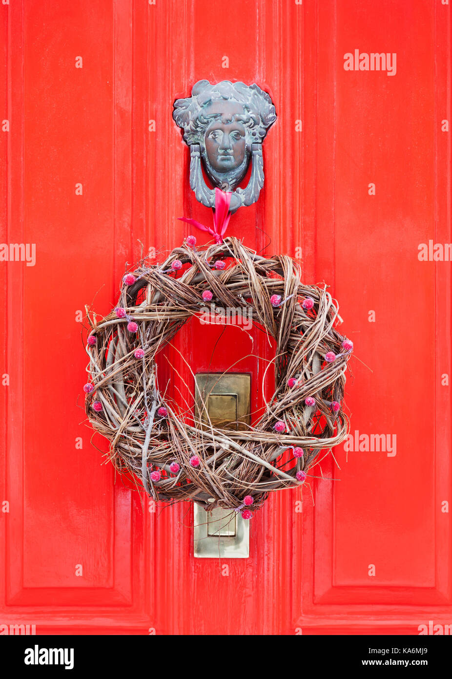 Natürliche Weihnachten Kranz hängen von einem reich verzierten Klopfer eine helle rote Tür. Stockfoto
