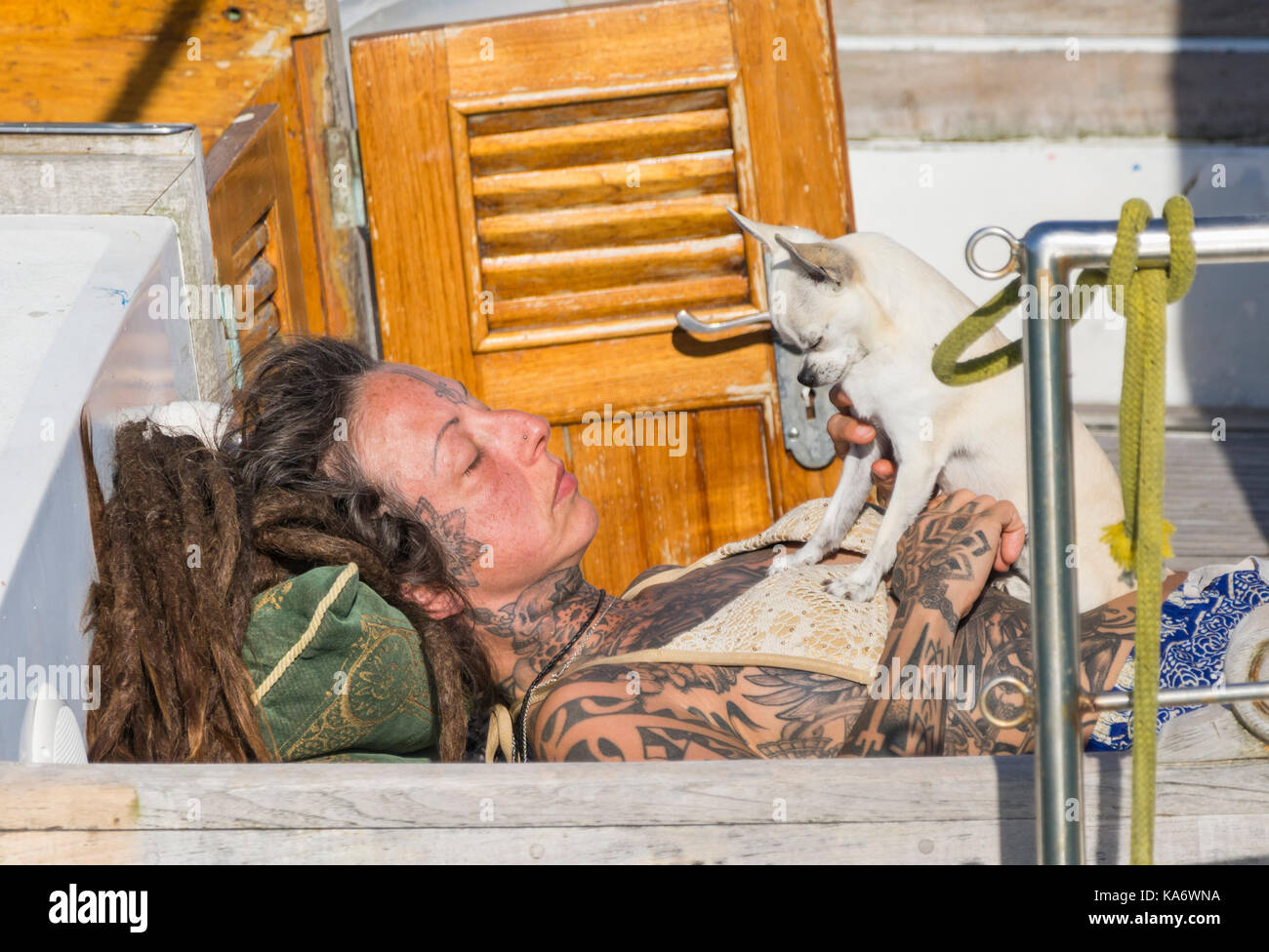 Frau mit Tattoos auf einem Boot in der Sonne mit einem Hund. Stockfoto