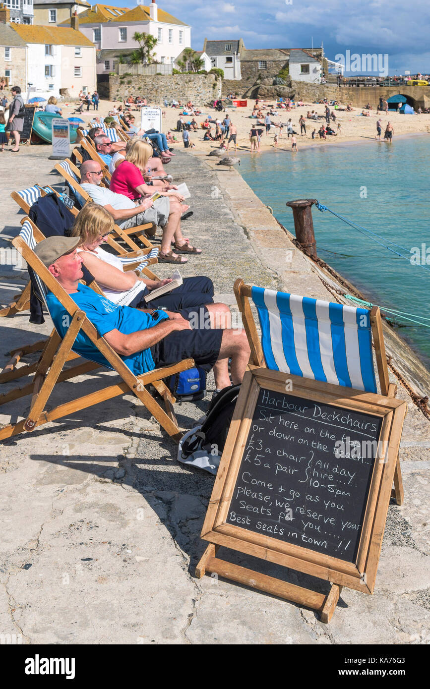 St Ives - Urlauber entspannen in Liegestühlen auf dem Kai am Hafen Strand St Ives Cornwall. Stockfoto