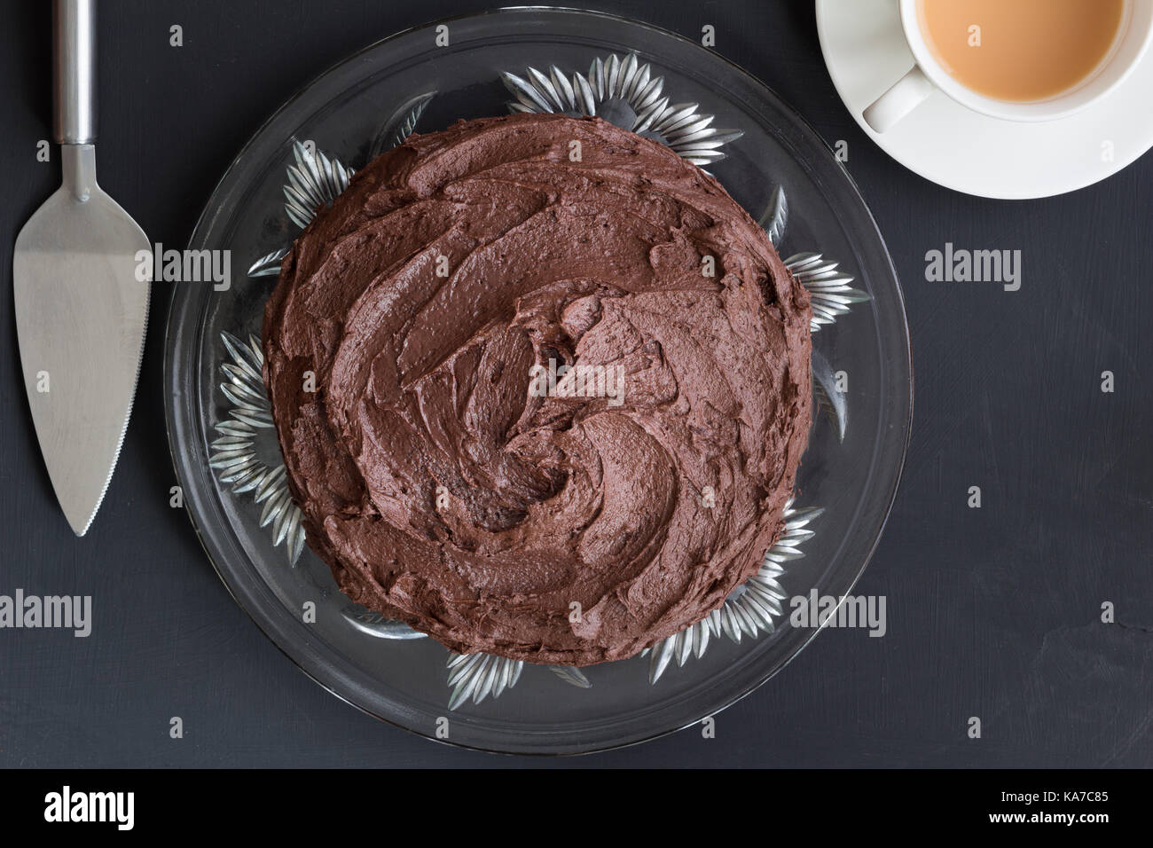 Choclolate Kuchen auf Glasplatte mit Silver Server und Tasse Tee auf schwarzem Hintergrund - Ansicht von oben Stockfoto