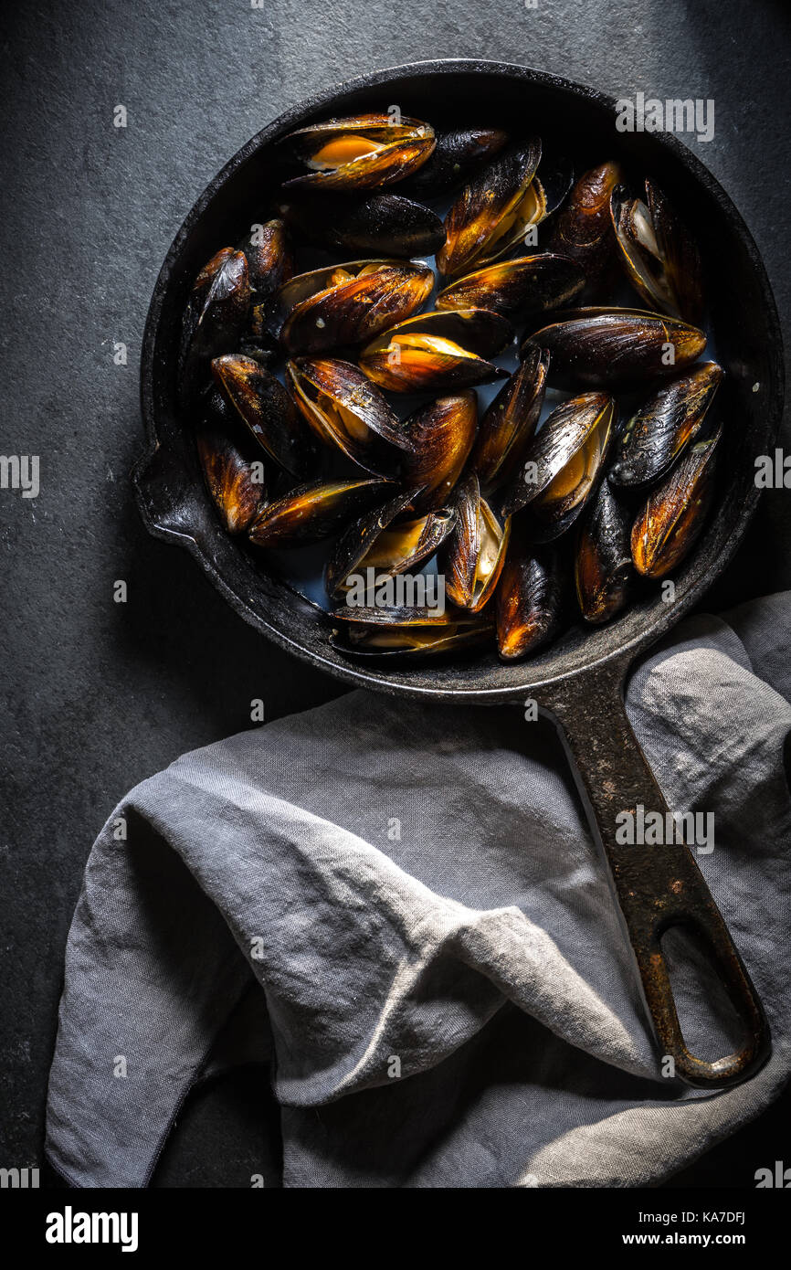 Muscheln auf einer gusseisernen Pfanne und Serviette auf einem grauen Hintergrund vertikal Stockfoto
