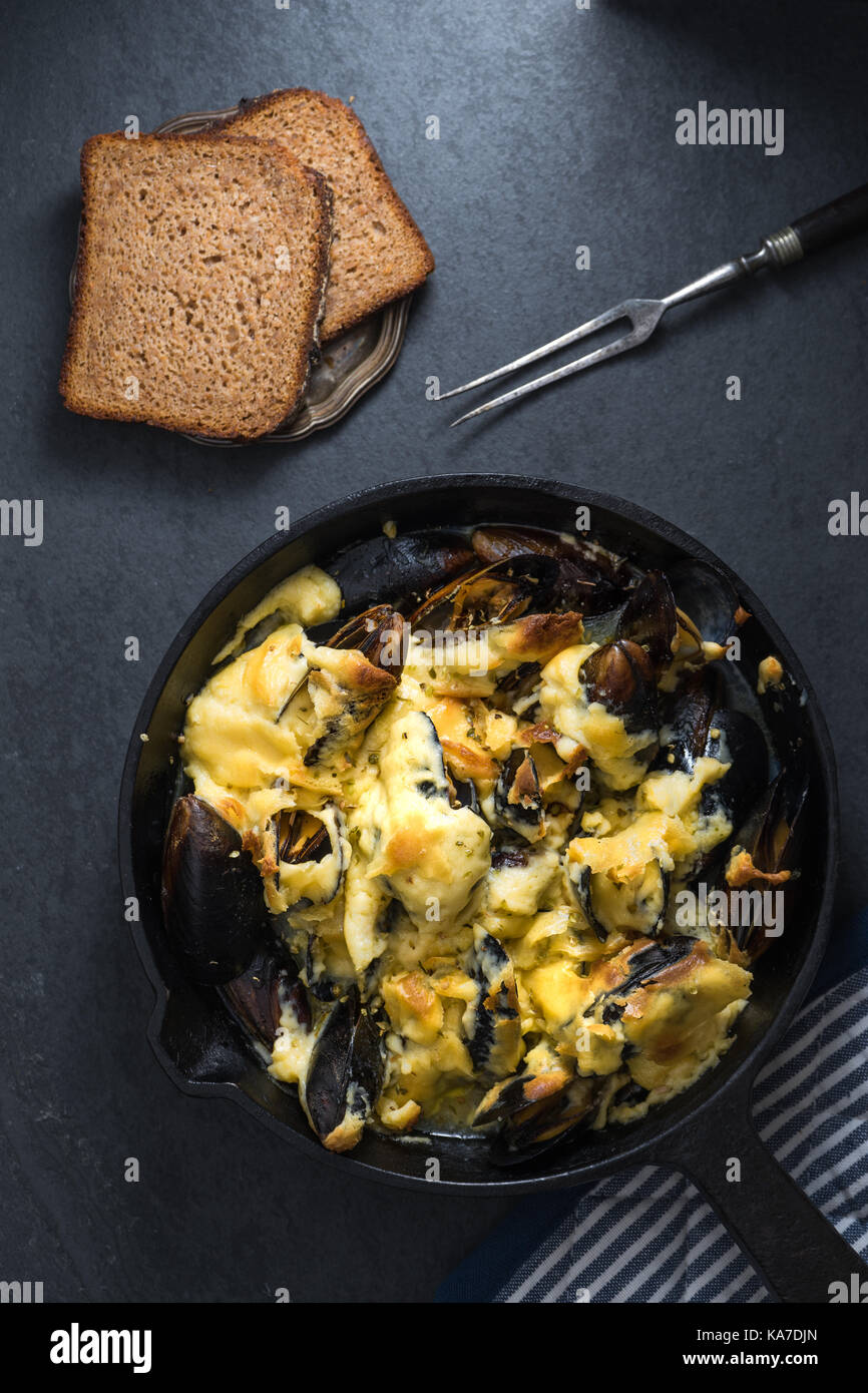 Miesmuscheln mit Käse Sauce in einer Pfanne, Serviette und Gabeln, Brot vertikale Stockfoto