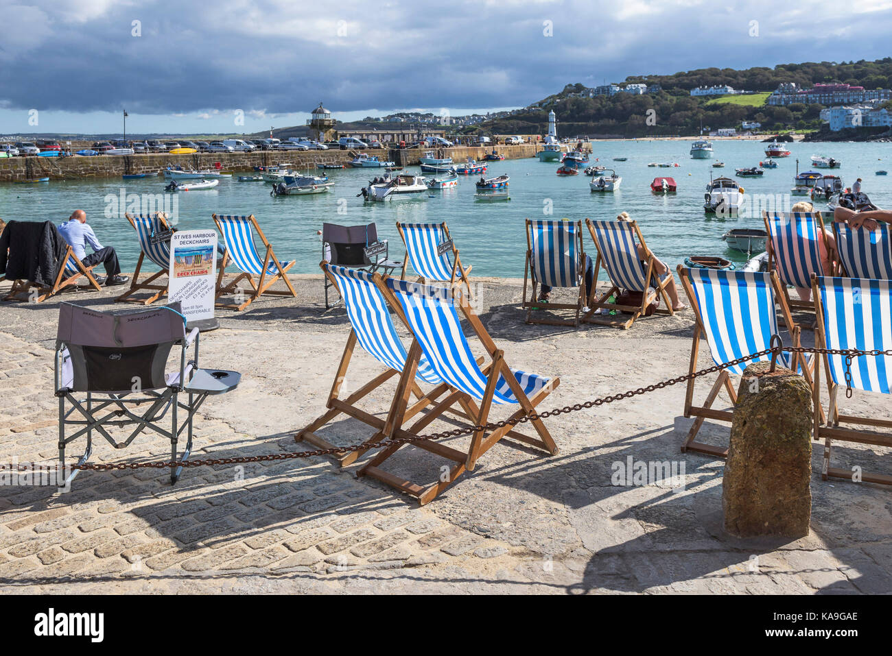 St Ives - Liegestühle auf dem Kai mit Blick auf den Hafen von St Ives in Cornwall. Stockfoto