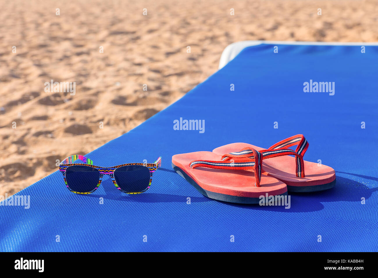 Badeschlappen und Sonnenbrille auf Blau Sonnenliege am Strand Stockfoto
