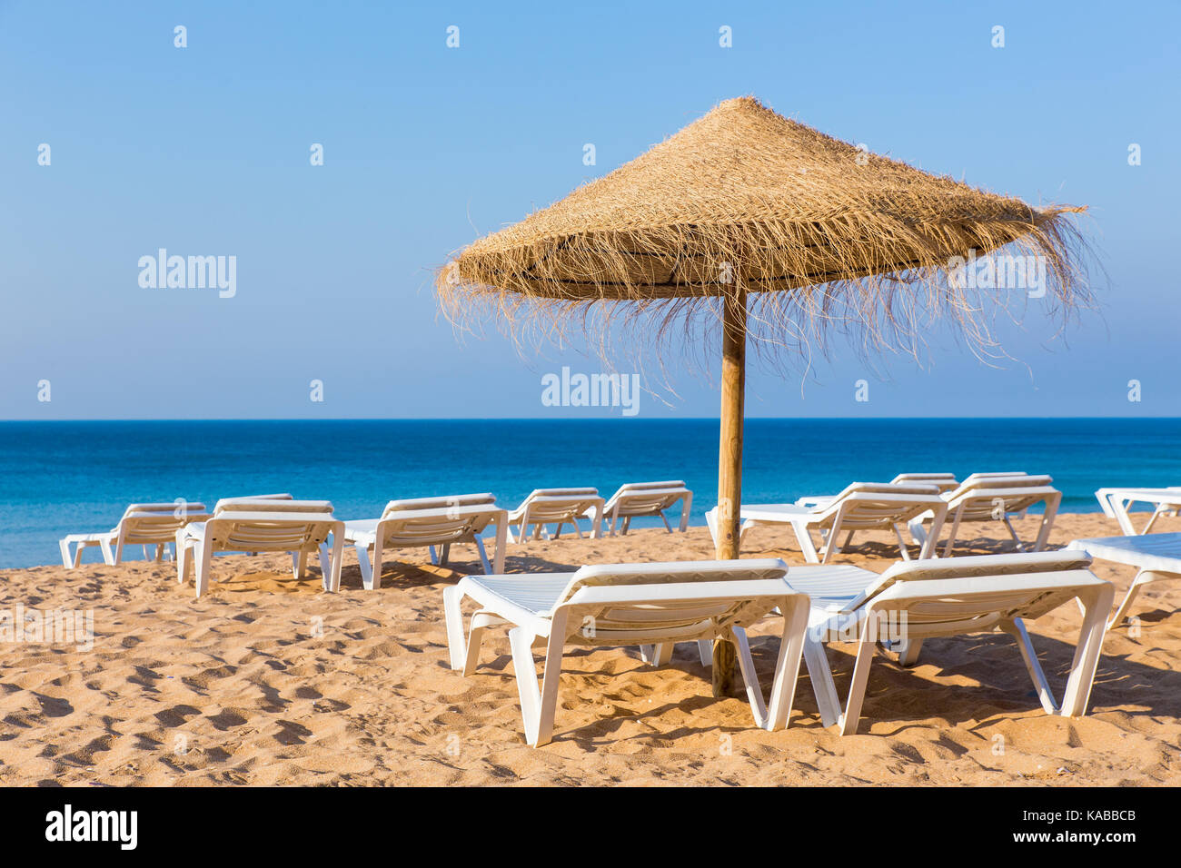 Wicker Strand Sonnenschirm mit Liegestühlen am blauen Meer Stockfoto