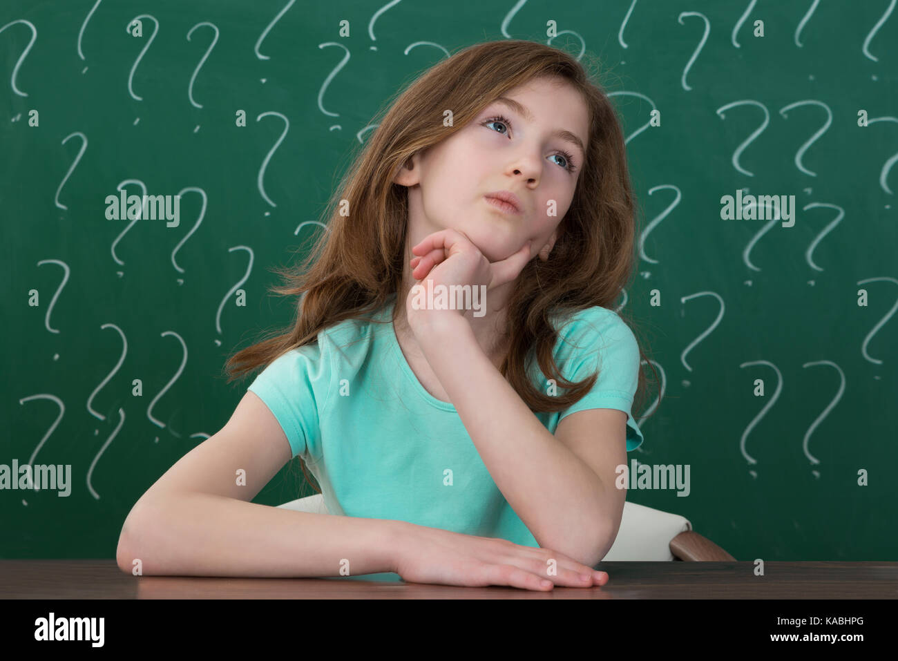 Betrachten Mädchen sitzen am Schreibtisch mit Fragezeichen gezeichnet Mit Kreide an die Tafel Stockfoto