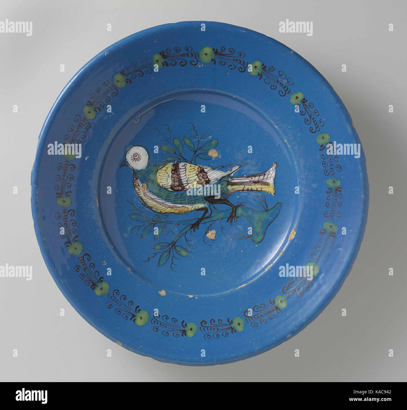 Dieser farbenfrohe Teller ist mit einem Vogel verziert, der auf einem Ast sitzt und von Punkt- und Spiralmustern entlang seines Randes umgeben ist. Es repräsentiert traditionelle dekorative Kunst mit einem Fokus auf lebendige Motive und detailgetreue Handwerkskunst. Stockfoto