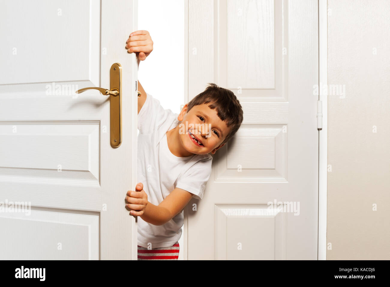 Kleiner Junge schaut hinter Tür mit Lächeln Stockfoto