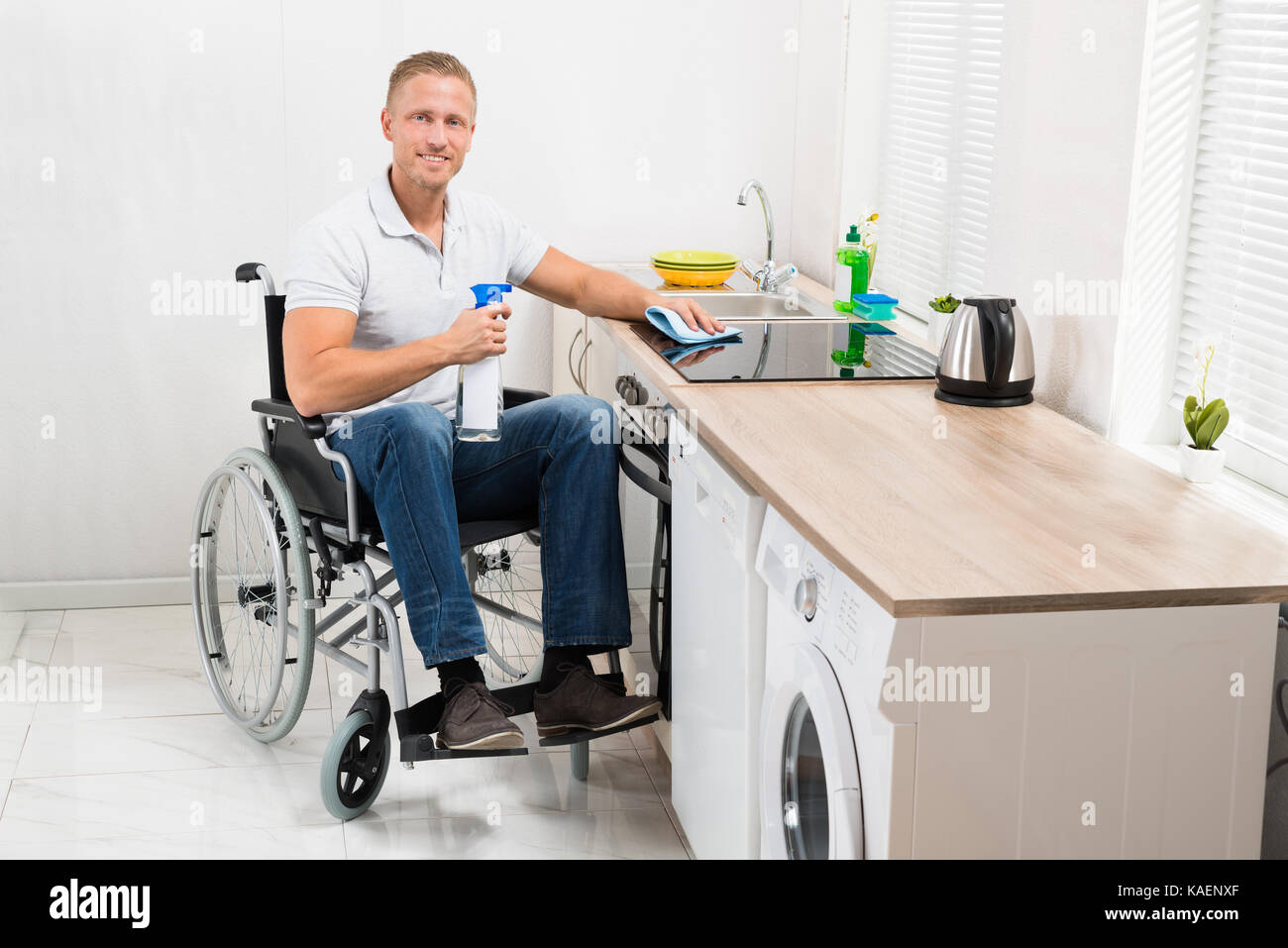 Junge glücklich Mann auf Rollstuhl Reinigung Induktion Herd in der Küche Zimmer Stockfoto
