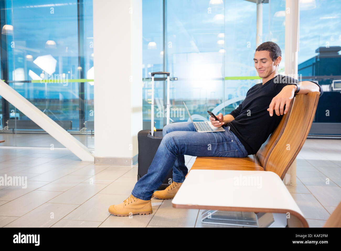 Junger Mann mit Handy und Laptop am Flughafen Stockfoto