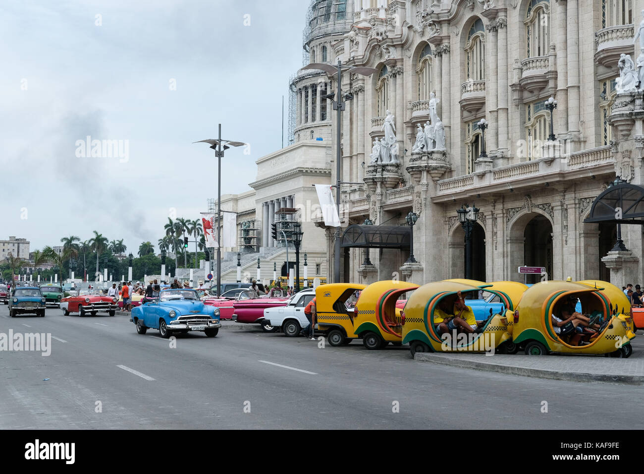 Taxis warten am Straßenrand im Parque Central als Oldtimer vorbei in Havanna, Kuba. Stockfoto