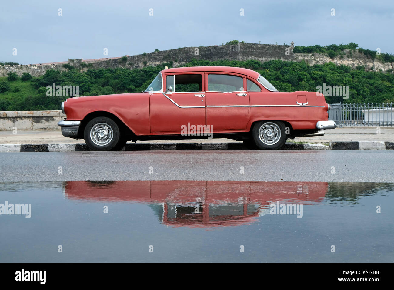Ein Oldtimer ist in einem Pool von Regenwasser auf dem Malecón in Havanna, Kuba widerspiegelt, nach einem großen Regen Sturm. Stockfoto