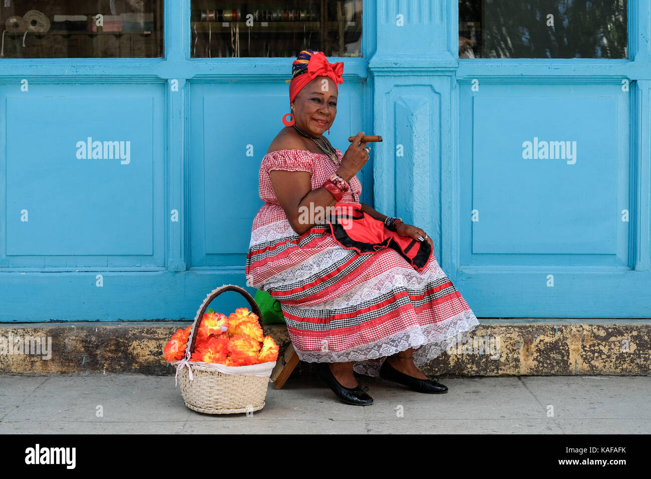 Ein farbenfroh gekleideten kubanische Frau in traditioneller Kleidung sitzt auf den Straßen von Habana Vieja in Havanna, Kuba. Stockfoto