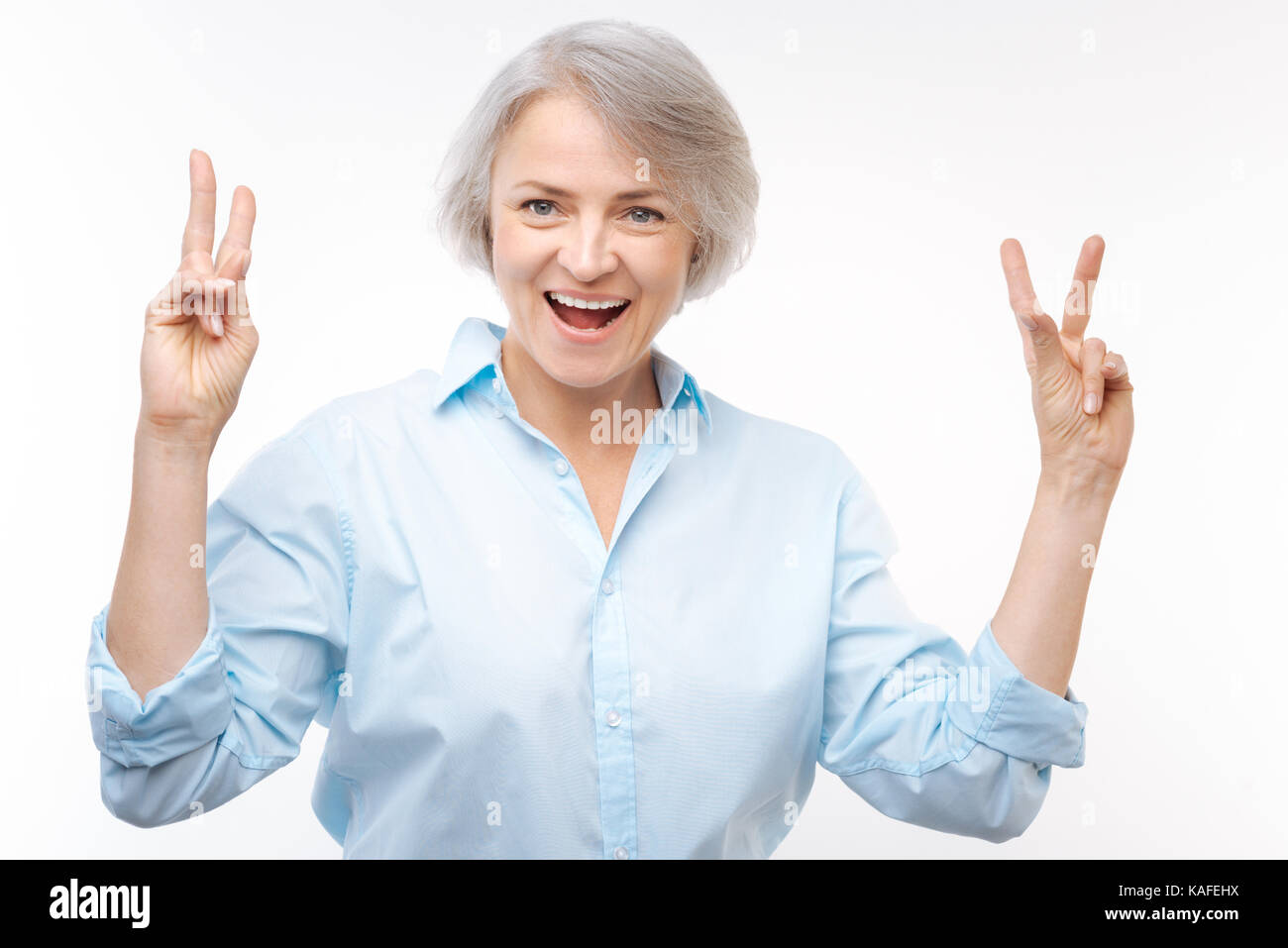 Fröhliche grauhaarige Frau, v-Zeichen mit beiden Händen Stockfoto
