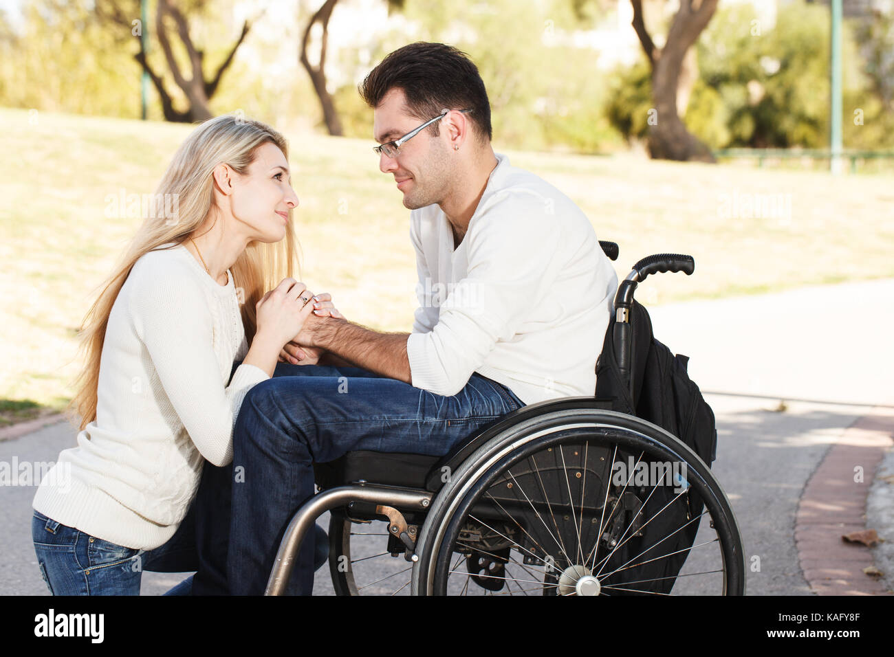 Mädchen vor ihrem behinderten Freund sitzt in einem Rollstuhl im Park Stockfoto