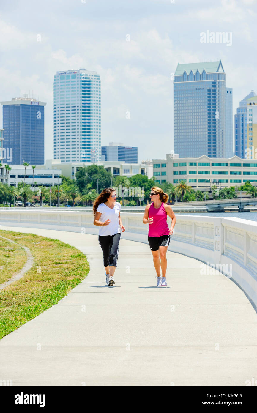 Zwei Frauen Joggen entlang der Bayshore Boulevard mit der Innenstadt von Tampa, Florida, USA Skyline im Hintergrund. Stockfoto