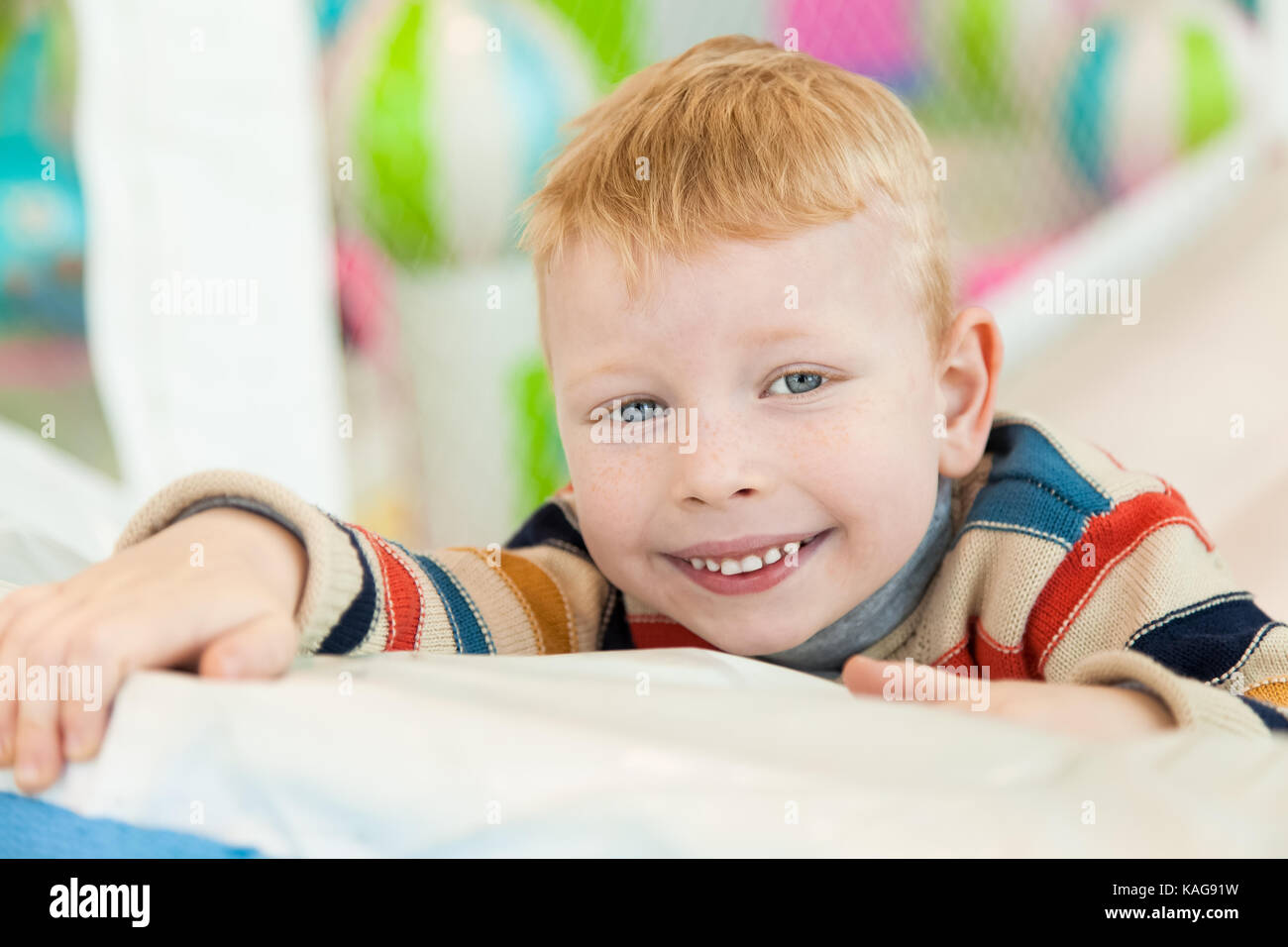 Ein kleiner Junge, der auf dem Boden liegt und von einem bunten Ballon umgeben ist Stockfoto