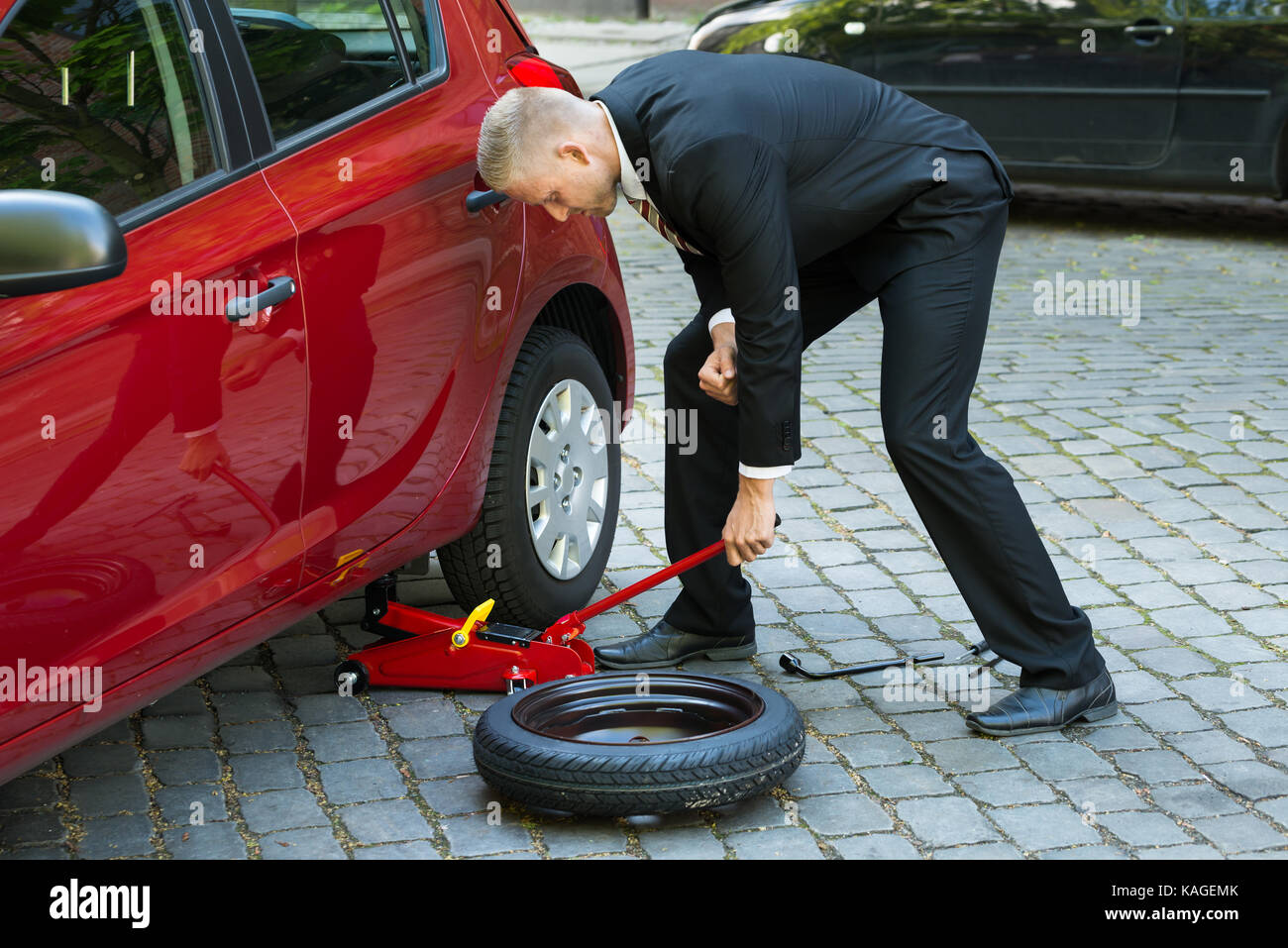 Mann, der versucht, das Auto mit roten Hydraulische Wagenheber für die Instandsetzung Stockfoto