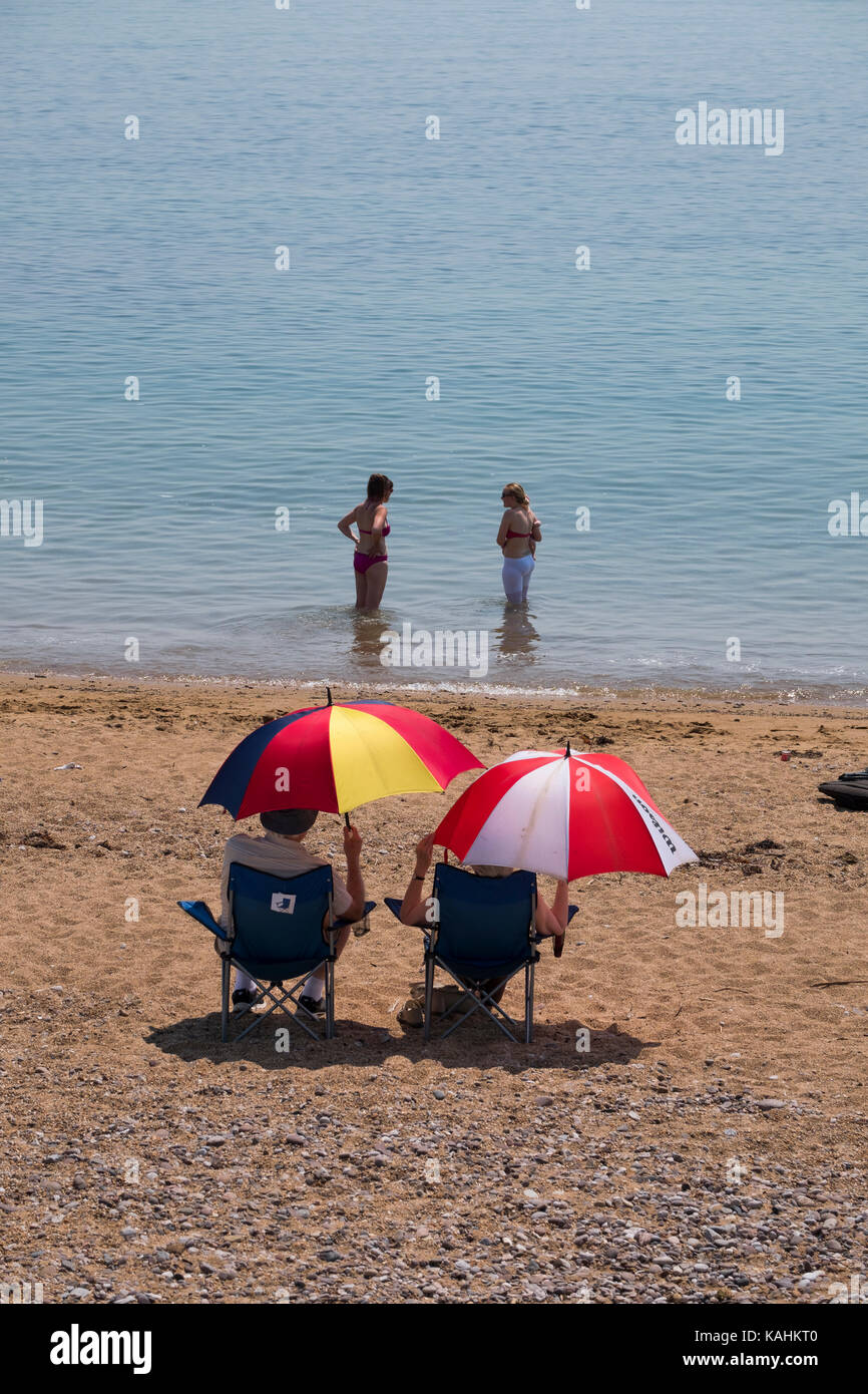 Menschen unter Sonnenschirmen am Strand von West Bay, Dorset, Großbritannien. Stockfoto